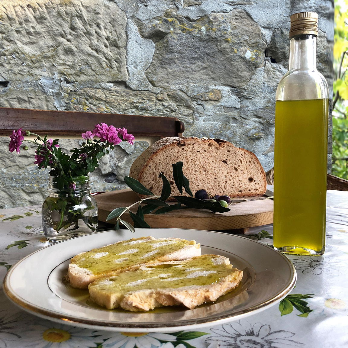 Tuscan bread drizzled with new olive oil, a bottle of oil and fresh olives on a country table